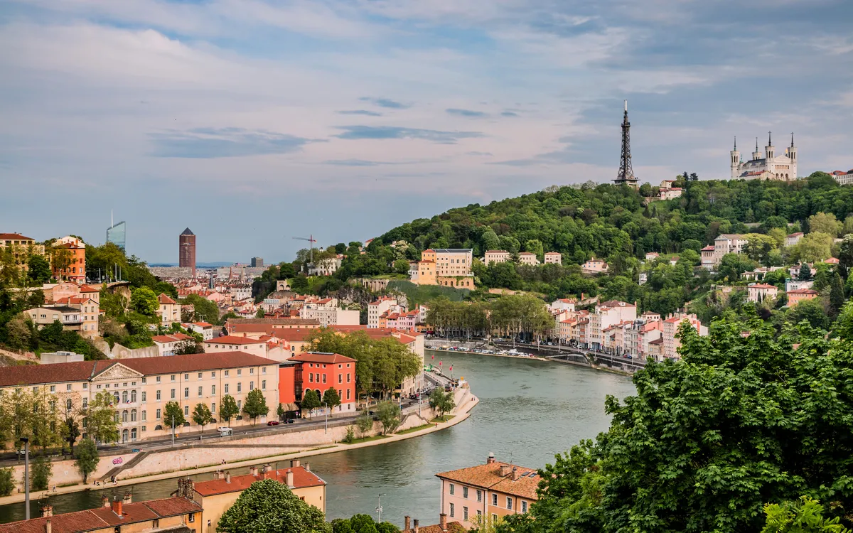 Stadtansicht mit Fluss, Hügel, Turm und alter Architektur.