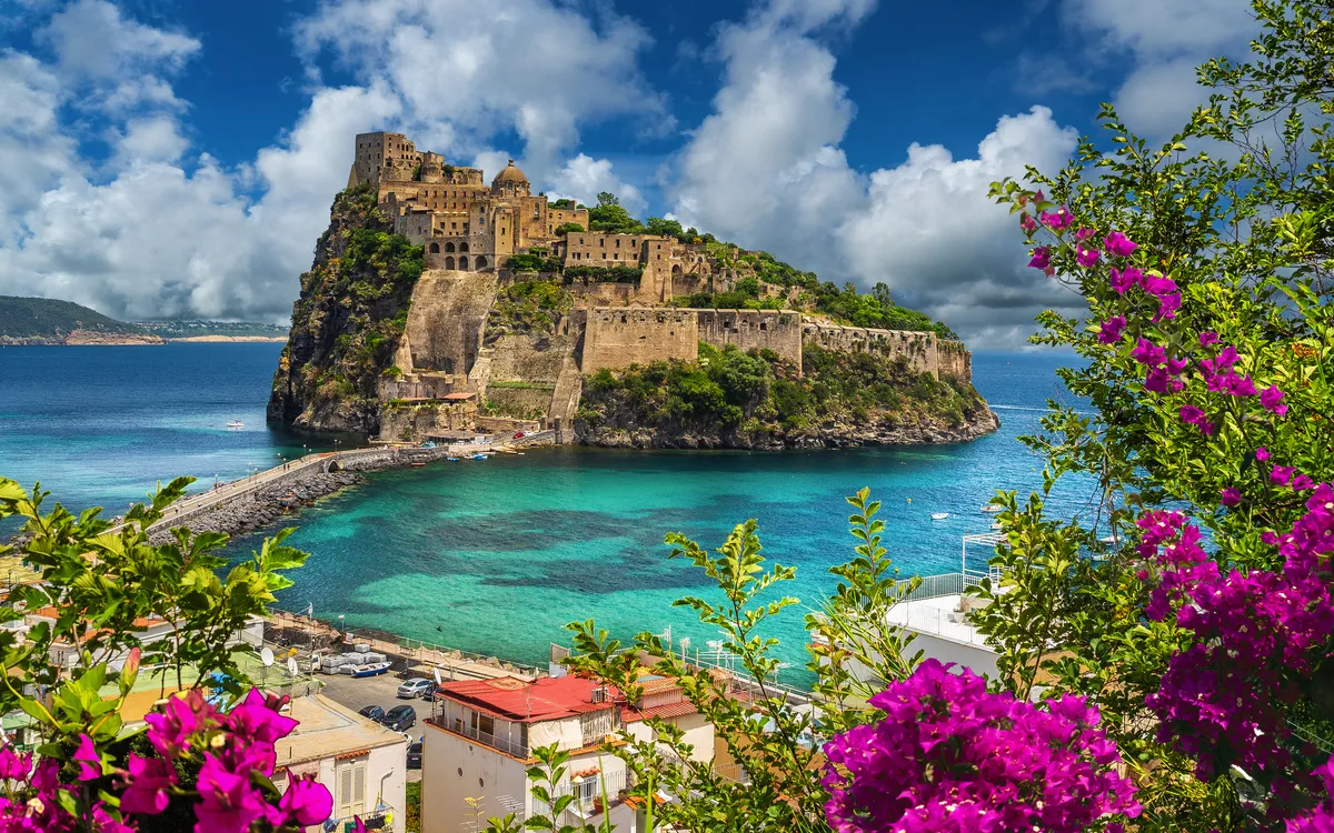 Mittelalterliche Festung auf einer Insel im türkisfarbenen Meer, umgeben von Blumen.