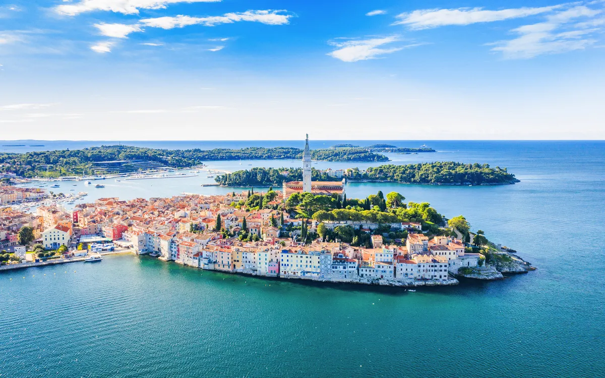 Küstenstadt an der Adria mit historischem Zentrum und Kirchturm, umgeben von Meer.