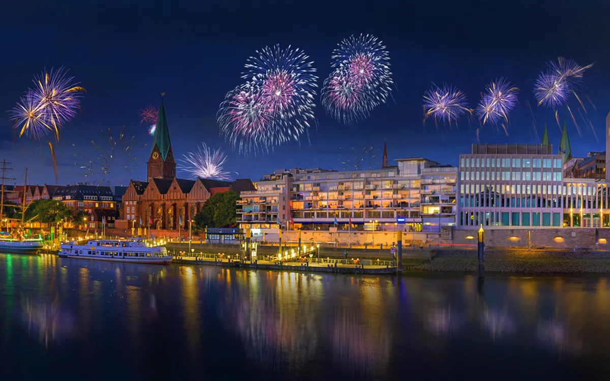 Feuerwerk über Bremen an Silvester mit beleuchteten Gebäuden am Flussufer.