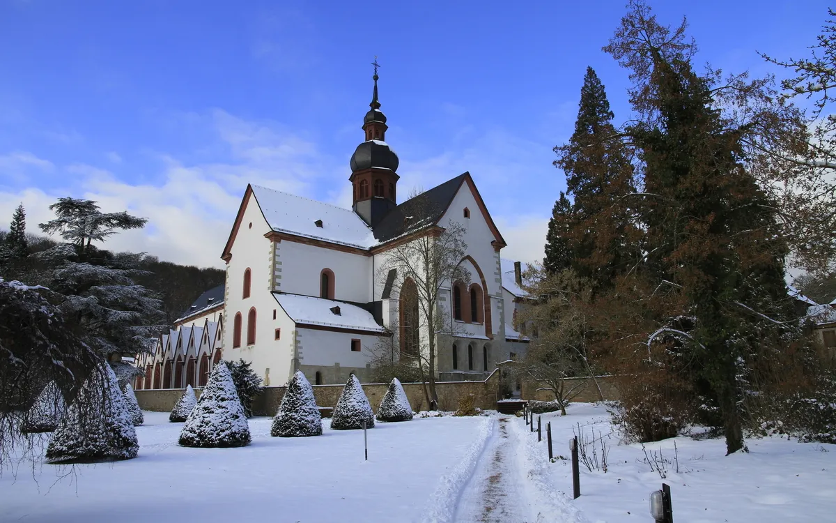 Kirche mit verschneitem Vorplatz und blauem Himmel im Hintergrund.