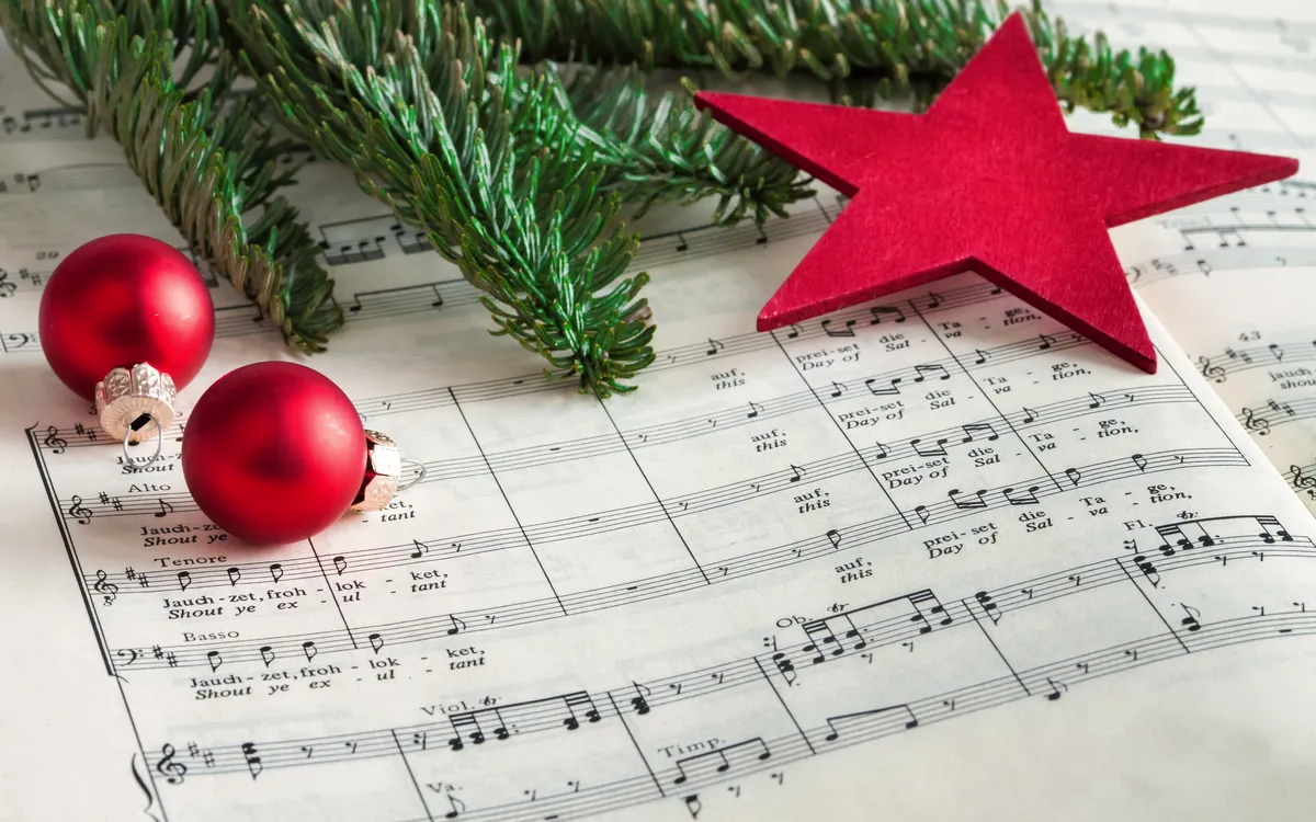Notenblätter mit roten Christbaumkugeln, Zweigen und Stern.