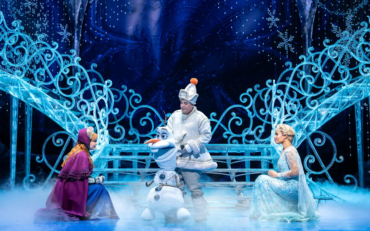 Drei Figuren in einem Eisschloss, darunter ein Schneemann, in einer Theateraufführung.