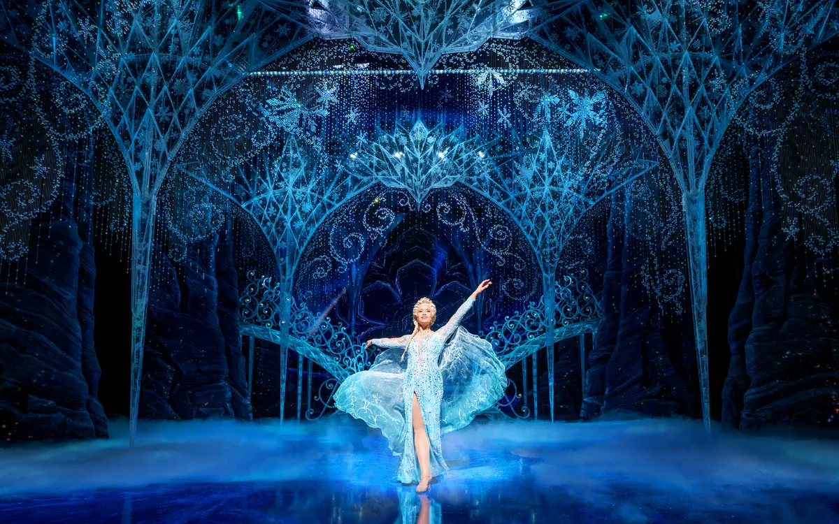 Frau in blauem Kleid auf eisiger, glitzernder Bühne in dramatischer Pose.