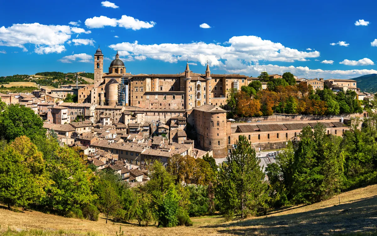 Stadtbild von Urbino in der Region Marken, Italien, mit malerischen Gebäuden und grüner Umgebung.