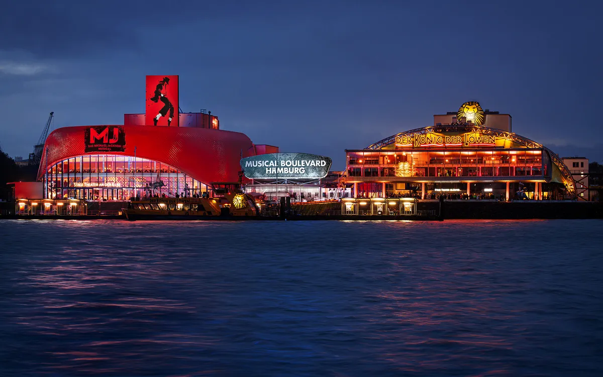 Musicaltheater in Hamburg bei Nacht, beleuchtet am Wasser.