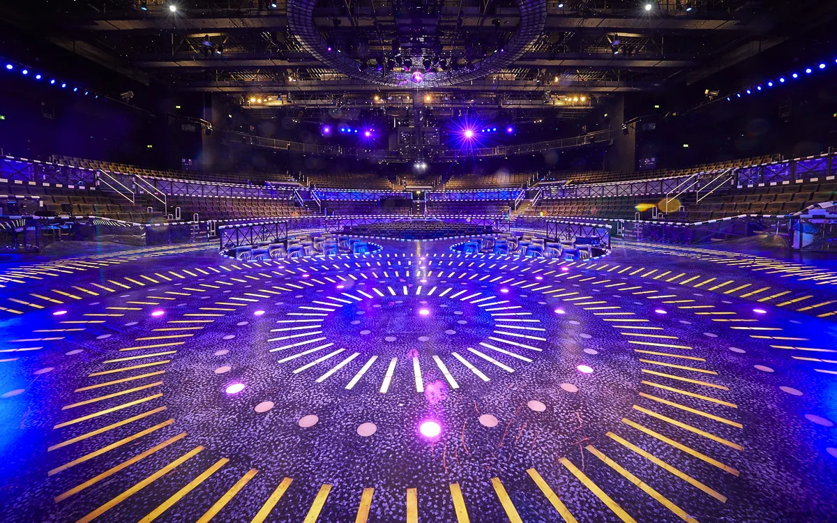 Bühne mit leuchtendem, kreisförmigem Muster und blauer Beleuchtung in einer Arena.