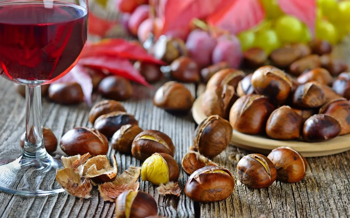 Kastanien, Trauben und ein Glas Rotwein auf Holztisch.