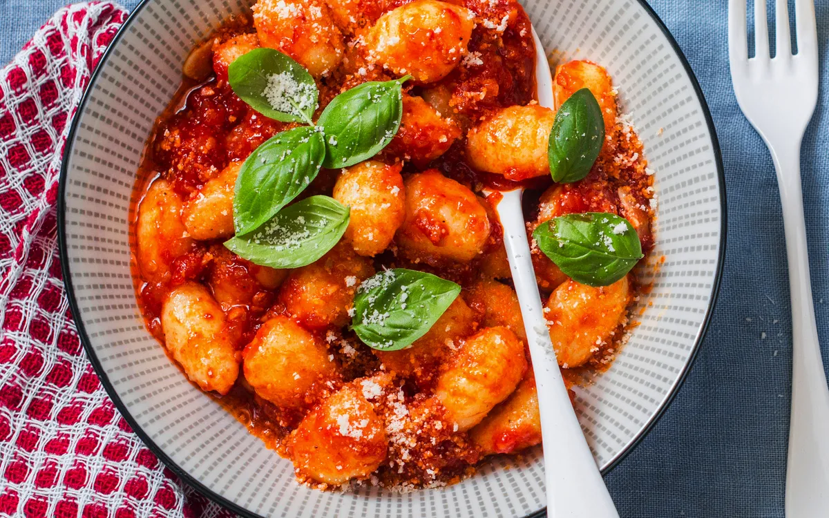 Gnocchi mit Tomatensauce und frischem Basilikum auf einem blauen Tuch.