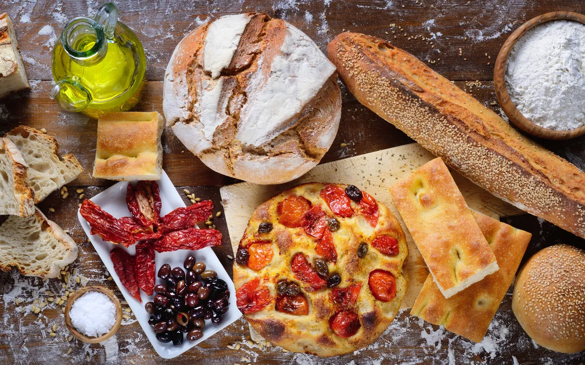 Verschiedene Backwaren mit Oliven, Tomaten und Olivenöl auf einem Holztisch.