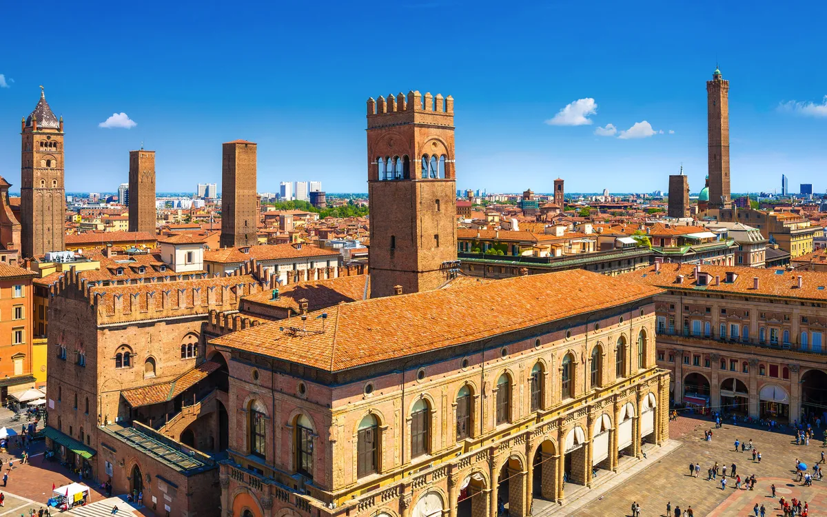 Stadtansicht von Bologna mit historischen Türmen und Plätzen bei klarem Himmel.