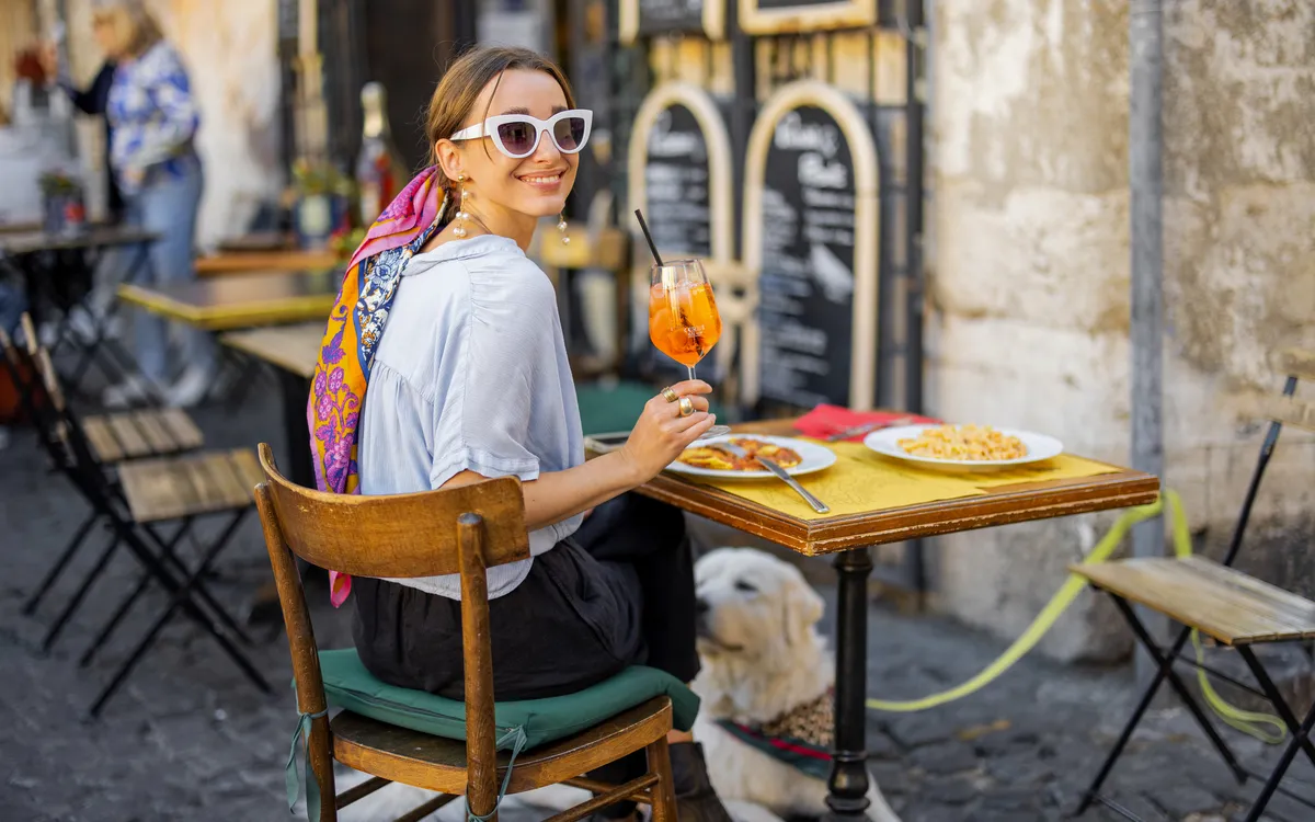 Frau sitzt in einem Bistro in Rom, isst italienische Pasta und trinkt einen Aperol Spritz.