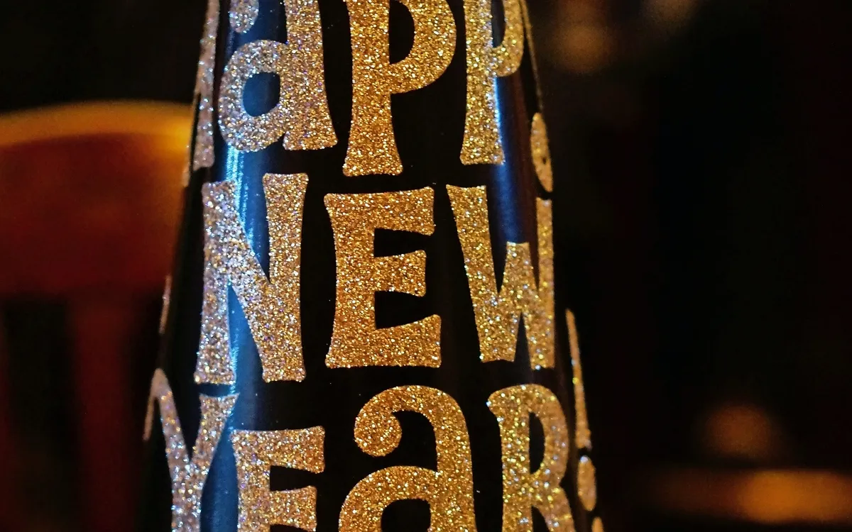 Schwarzer Partyhut mit glitzerndem Schriftzug "Happy New Year" im Vordergrund.
