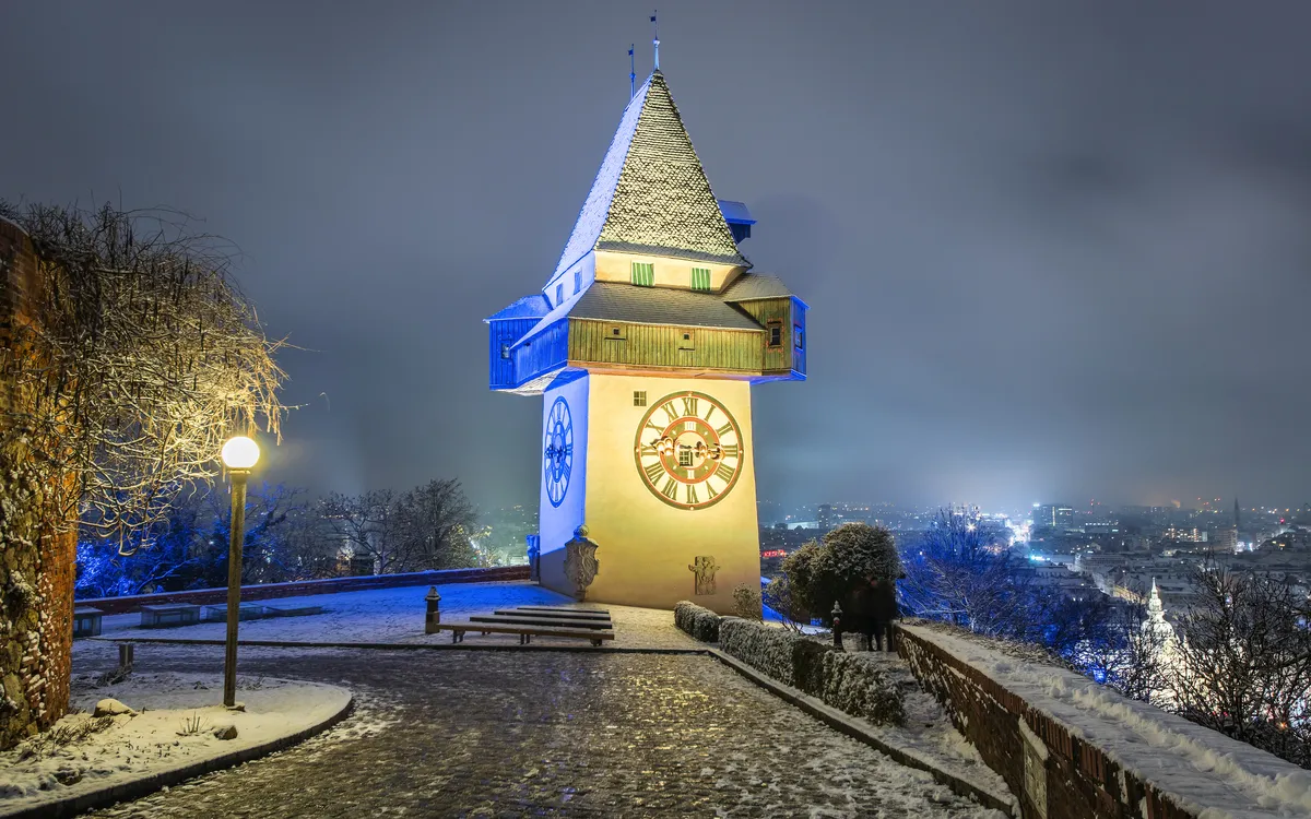 Uhrturm in Graz bei Nacht mit Schnee bedeckt.