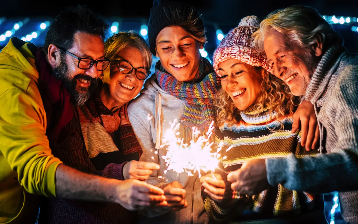 Gruppe fröhlicher Menschen mit Wunderkerzen im Freien bei Nacht.