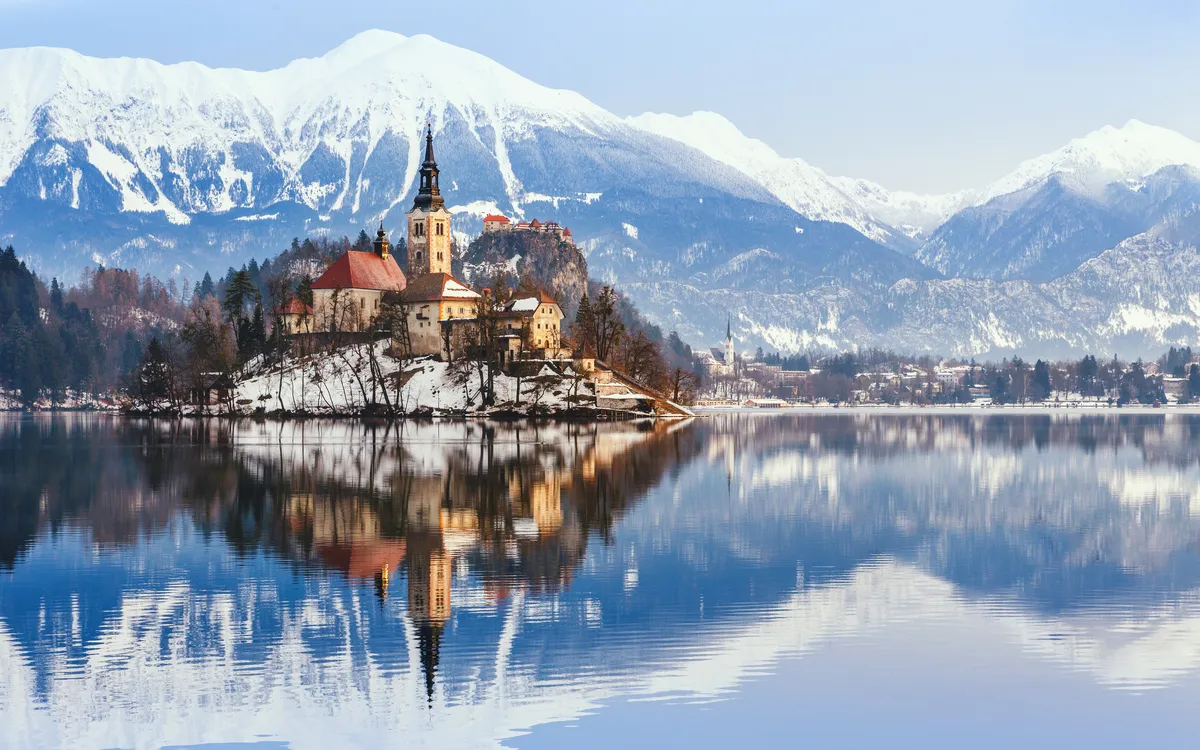 Kirche auf Insel in verschneiter Berglandschaft mit See.