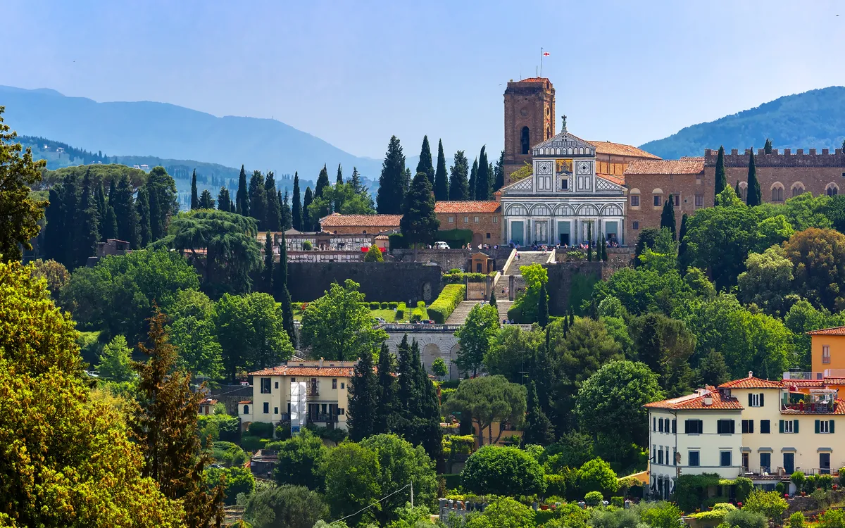 Basilika San Miniato al Monte auf einem Hügel in Florenz, umgeben von Bäumen.