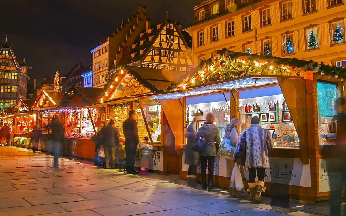 Weihnachtsmarktstände bei Nacht mit festlichen Lichtern und Menschen.