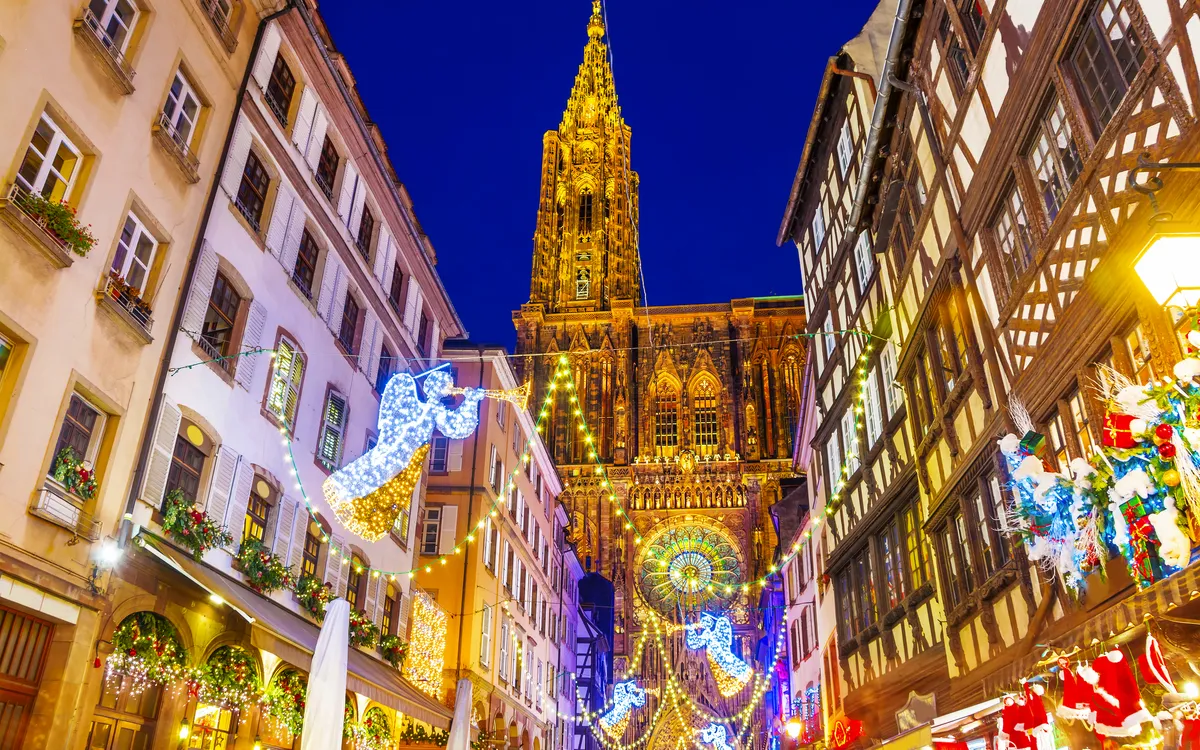 Straßenszene mit beleuchteter Kathedrale und Weihnachtsdekorationen am Abend.