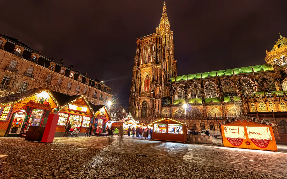 Weihnachtsmarkt bei Nacht vor beleuchteter Kathedrale.