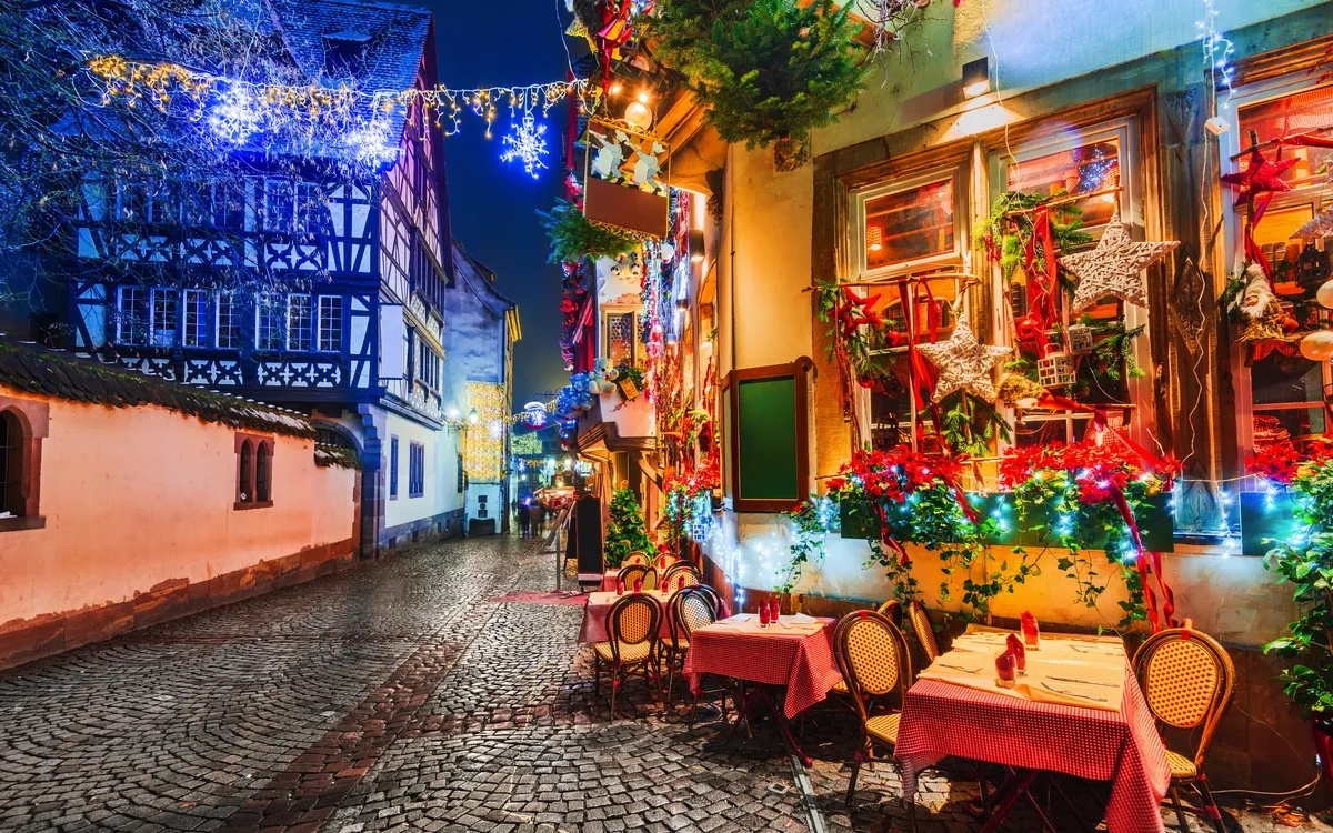 Beleuchtete, festliche Gasse mit Café und Fachwerkhäusern bei Nacht.