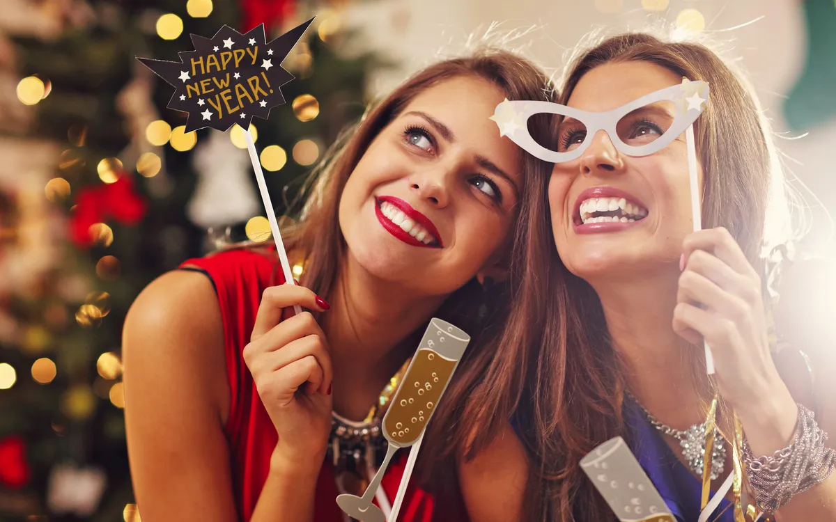 Zwei Frauen feiern lächelnd Silvester mit Partydekoration.