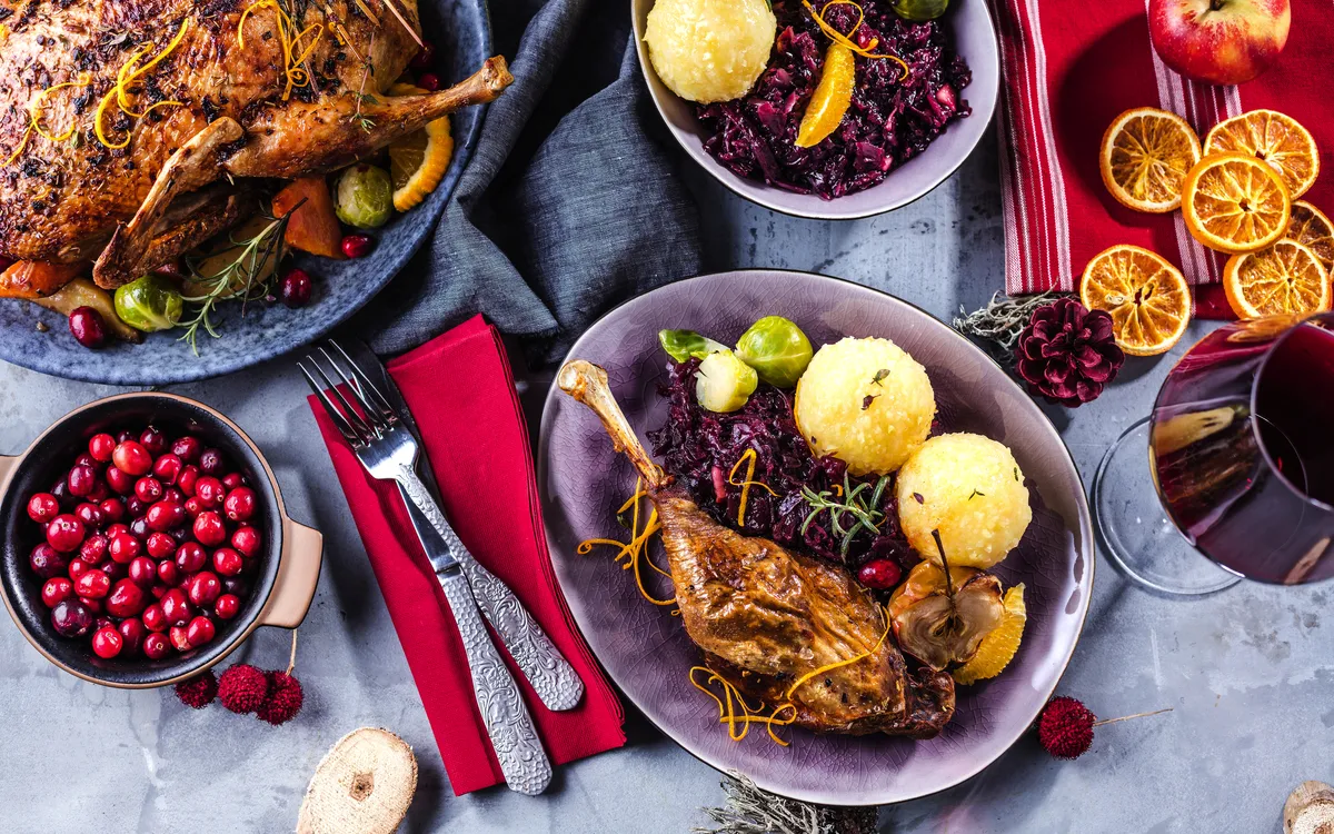 Festtagstisch mit Entenbraten, Rotkohl, Kartoffelklößen und roten Beeren.