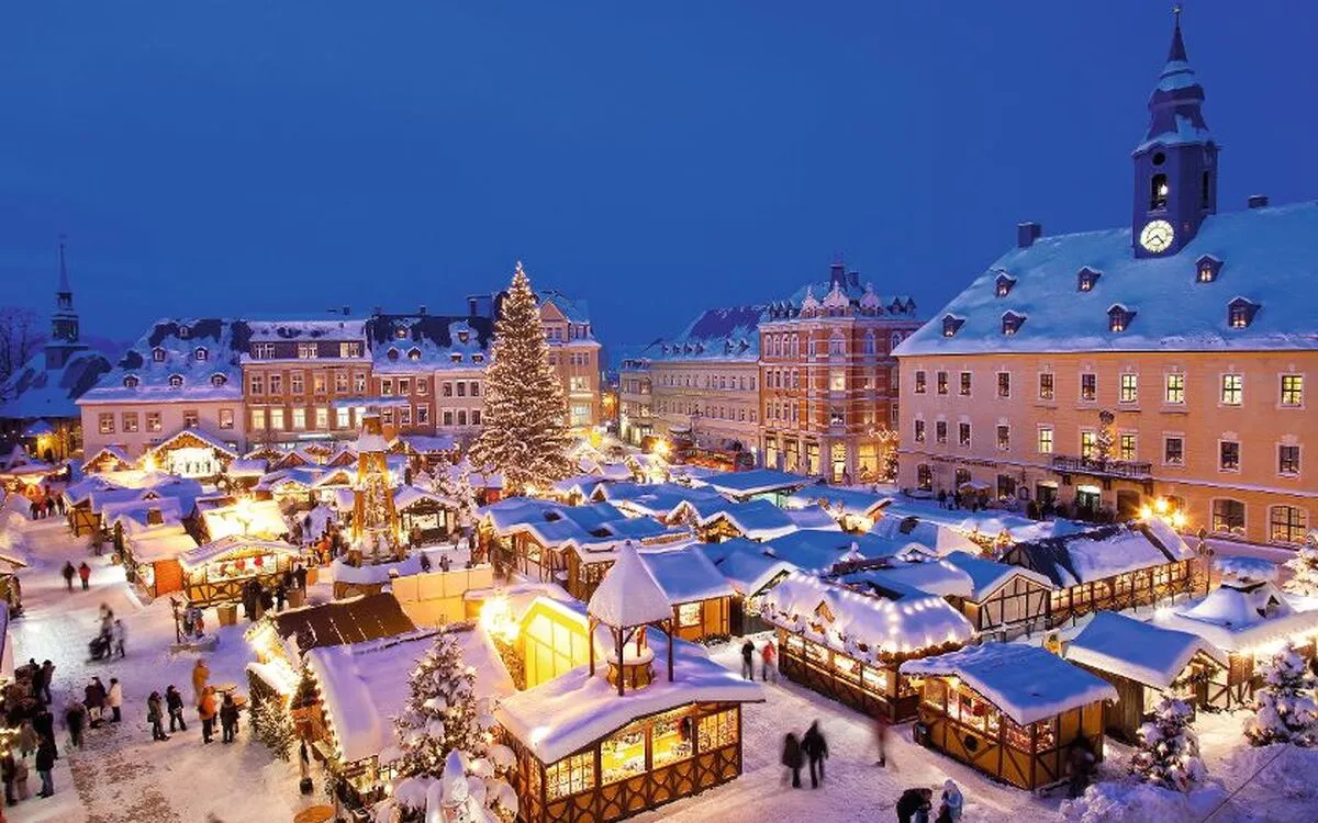 Weihnachtsmarkt bei Nacht mit beleuchteten Ständen und großem Weihnachtsbaum.