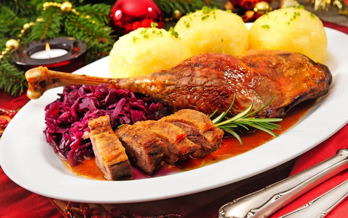 Festlicher Teller mit gebratener Gans, Rotkohl und Knödeln, dekoriert mit Tannenzweigen.