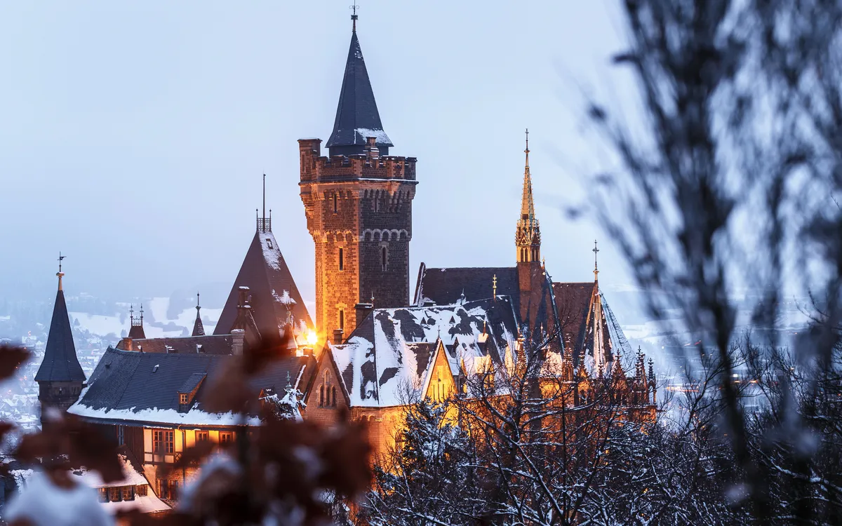 Mittelalterliches Schloss im Winter mit Schneebedeckung und abendlicher Beleuchtung.