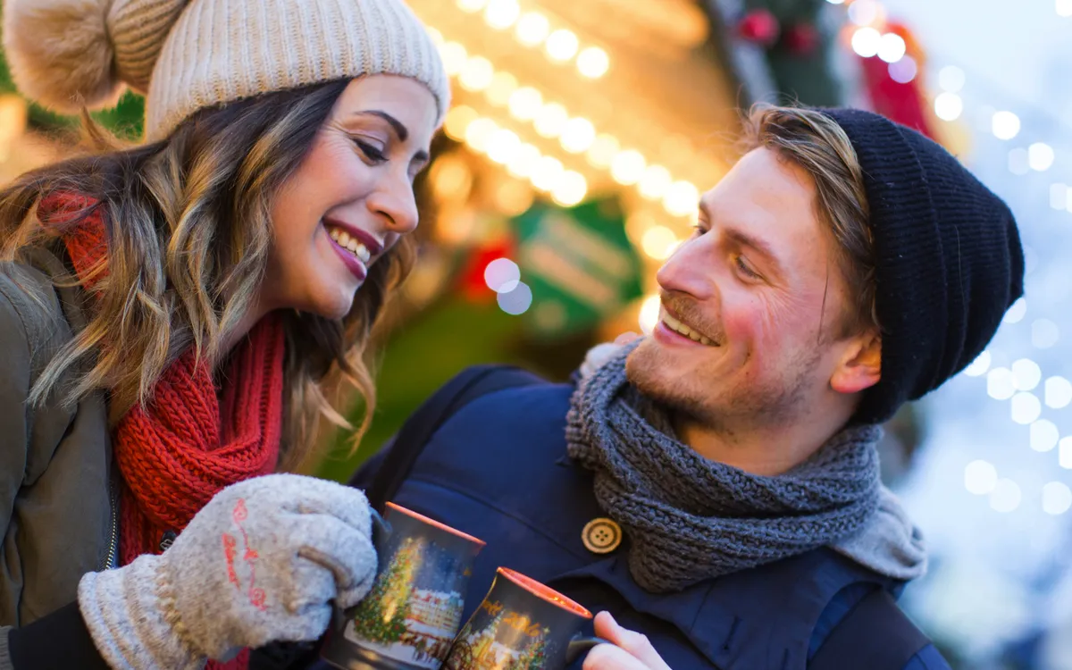 Paar lächelt und trinkt heißen Glühwein auf einem Weihnachtsmarkt.
