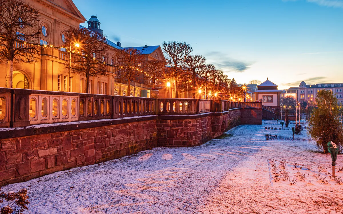 Historisches Gebäude bei Sonnenuntergang im Winter mit beleuchteten Bäumen und Schnee.