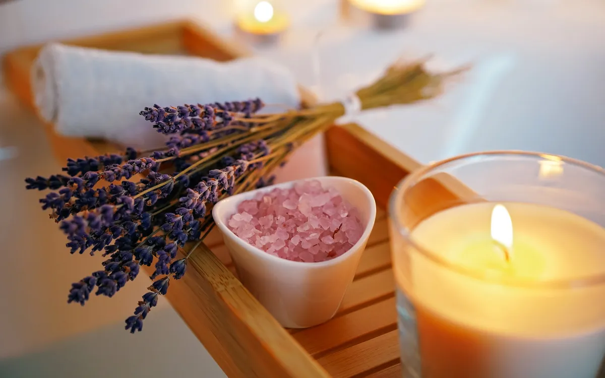 Lavendel, Badesalz, brennende Kerze auf Badewannenablage.