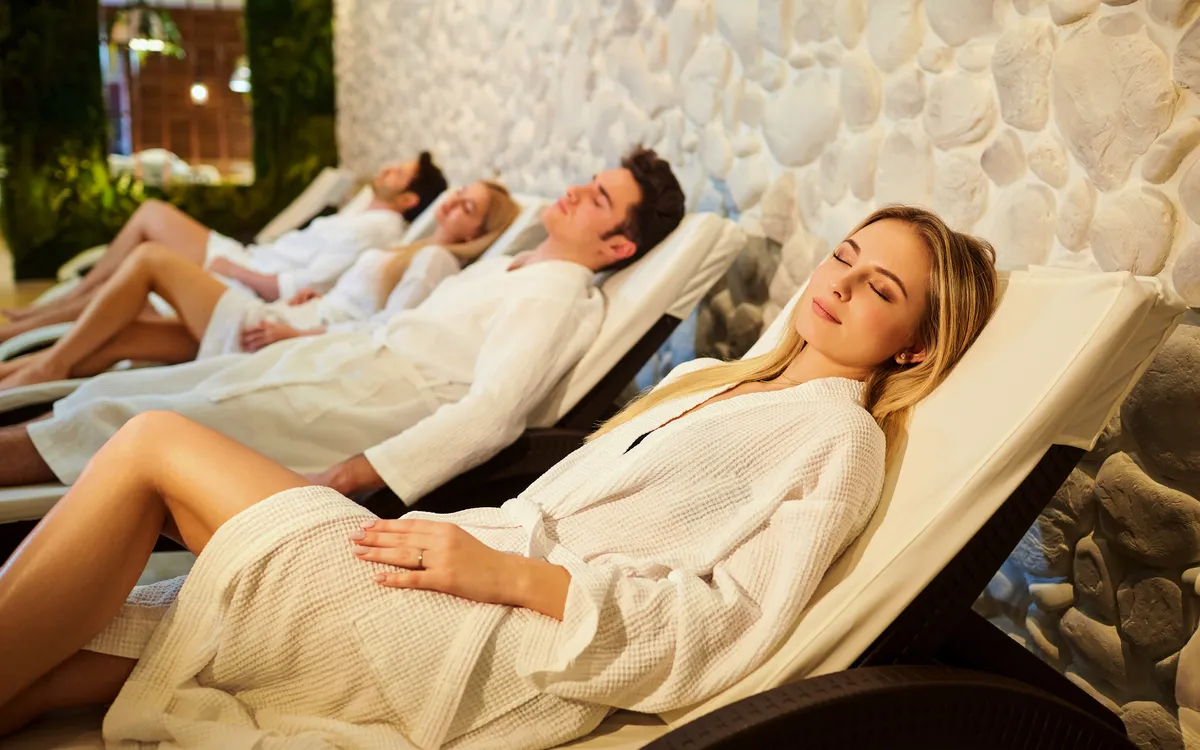 Personen in Bademänteln entspannen auf Liegestühlen in einem Spa.