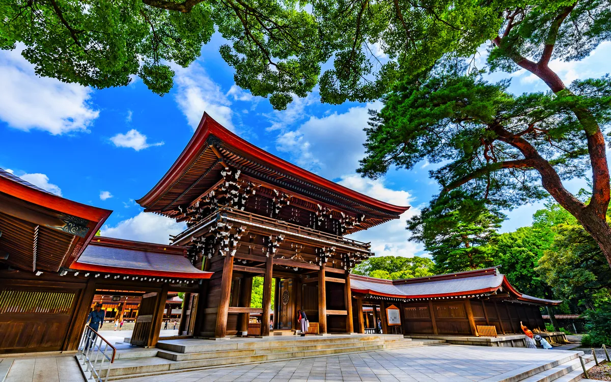 Holztor eines japanischen Schreins mit blauem Himmel und Bäumen im Hintergrund.