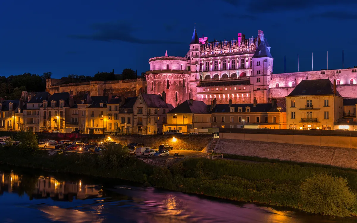 Schloss am Flussufer bei Nacht in stimmungsvoller Beleuchtung.
