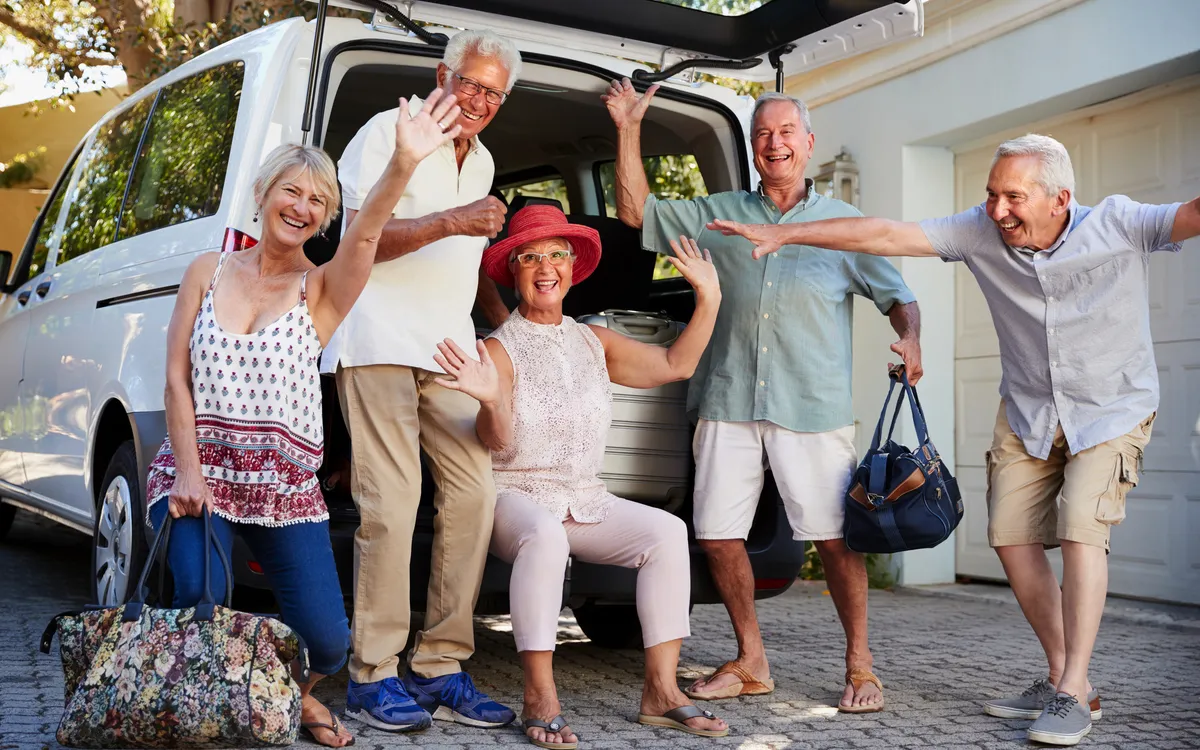 Seniorengruppe freut sich vor einem Auto auf einem Ausflug.