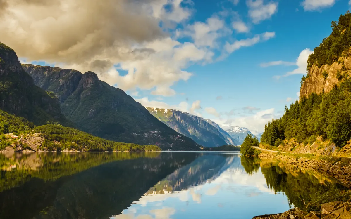Bergsee-Landschaft mit blauem Himmel und Wolken, gesäumt von bewaldeten Bergen.