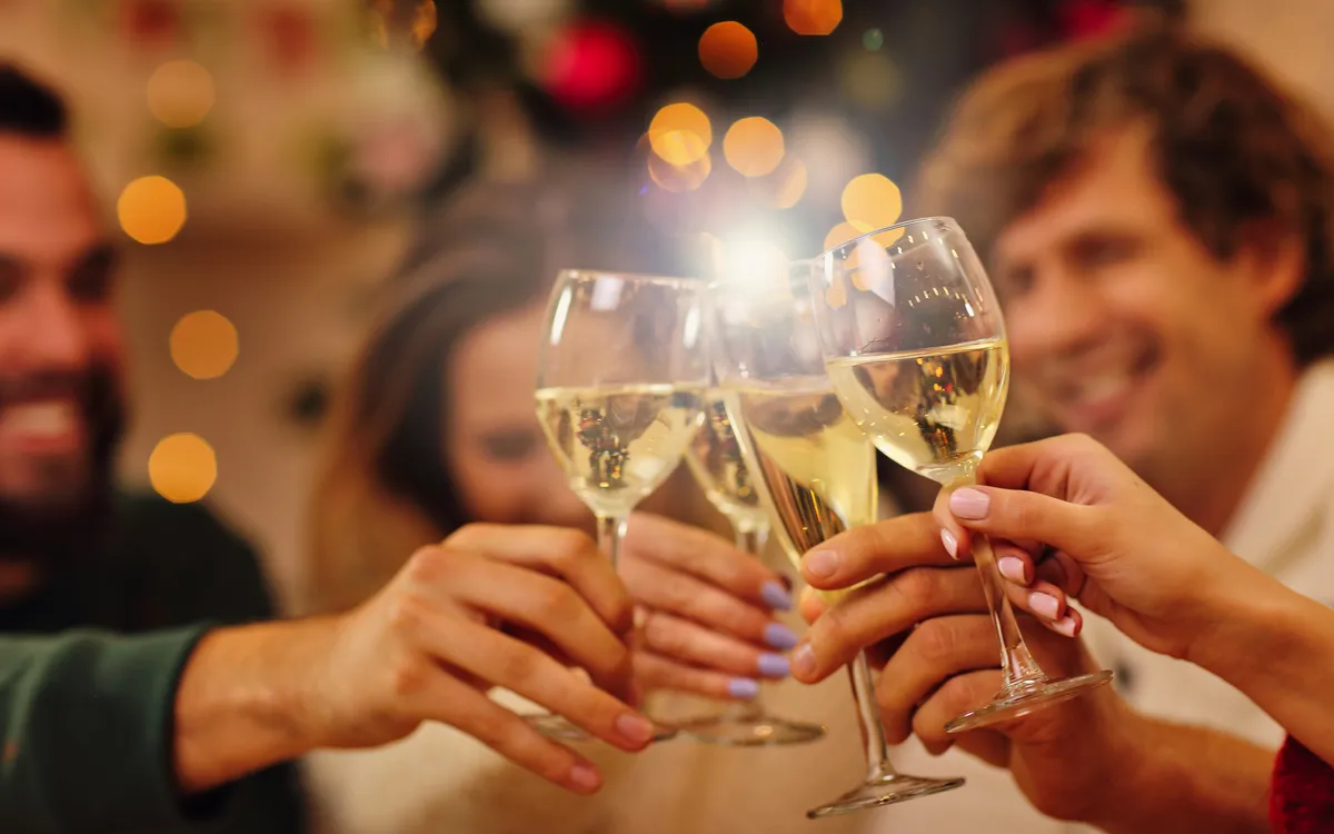 Gruppe von Freunden stößt mit Gläsern Sekt bei einer festlichen Weihnachtsfeier an.
