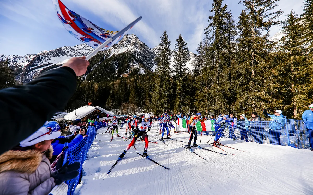 Langläufer im Wettkampf auf schneebedeckter Strecke, umgeben von Bergen und Wald.