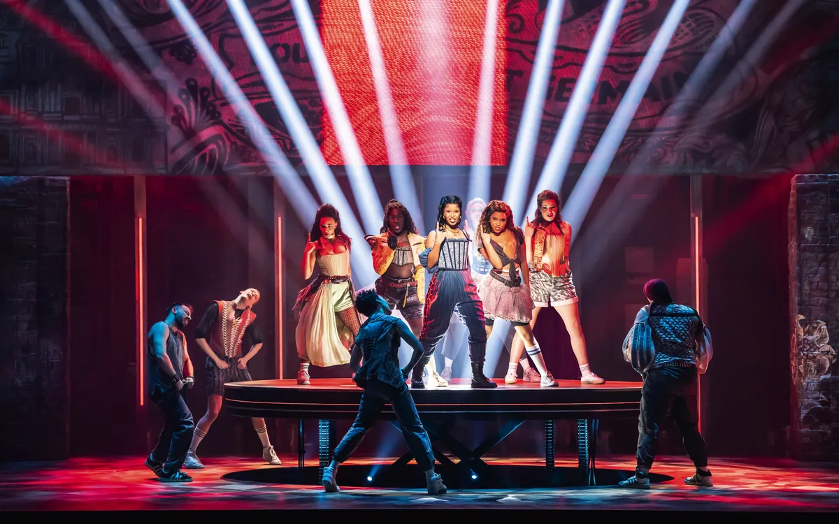 Szenenbild aus dem Musical "& Julia" in Hamburg mit Darstellern auf der Bühne in buntem Licht.