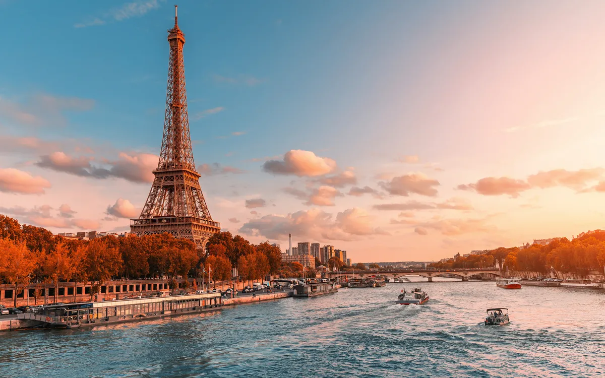 Der Eiffelturm in Paris bei Sonnenuntergang, mit der Seine im Vordergrund.