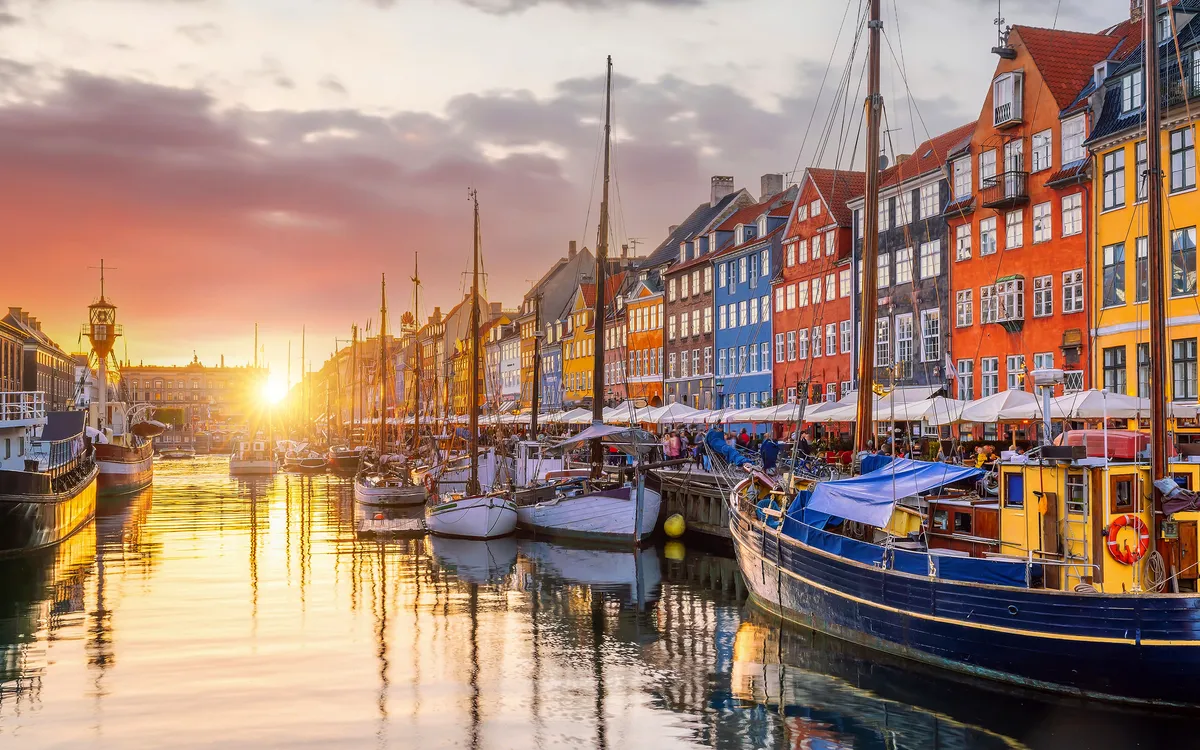 Hafen von Nyhavn in Kopenhagen bei Sonnenuntergang mit bunten Häusern und Segelbooten.