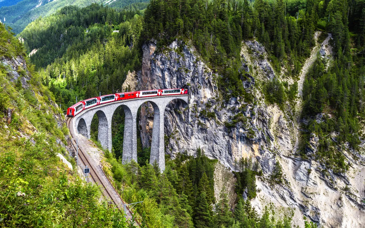Zug auf einem Viadukt in einer bewaldeten Berglandschaft