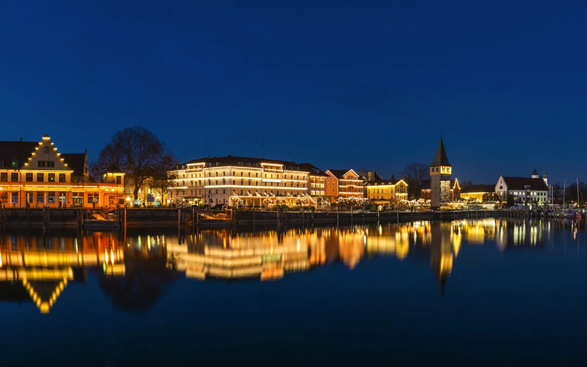 Nächtliche Hafenansicht mit beleuchteten Gebäuden und reflektierendem Wasser.