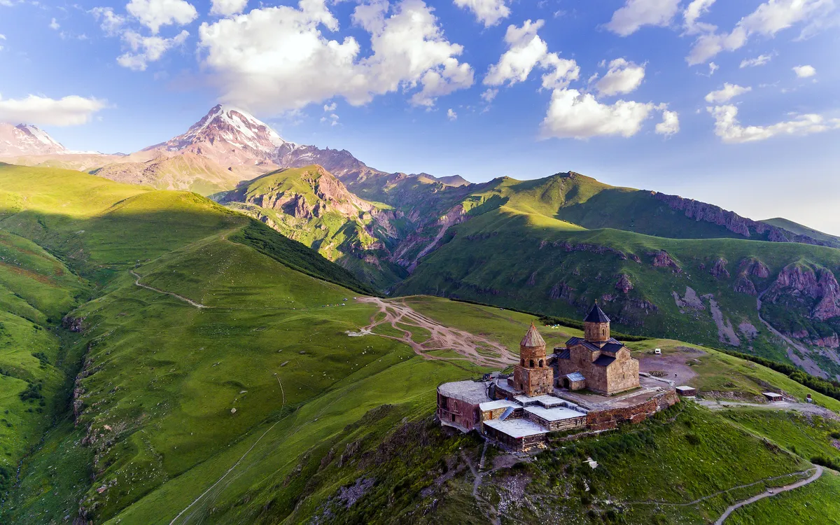 Bergkloster auf grünem Hügel mit Bergen im Hintergrund bei sonnigem Wetter