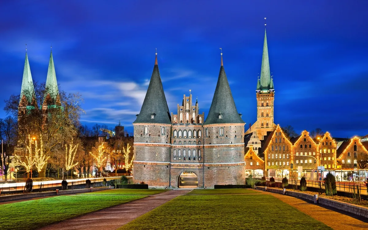 Holstentor in Lübeck bei Nacht mit beleuchteten Gebäuden im Hintergrund.
