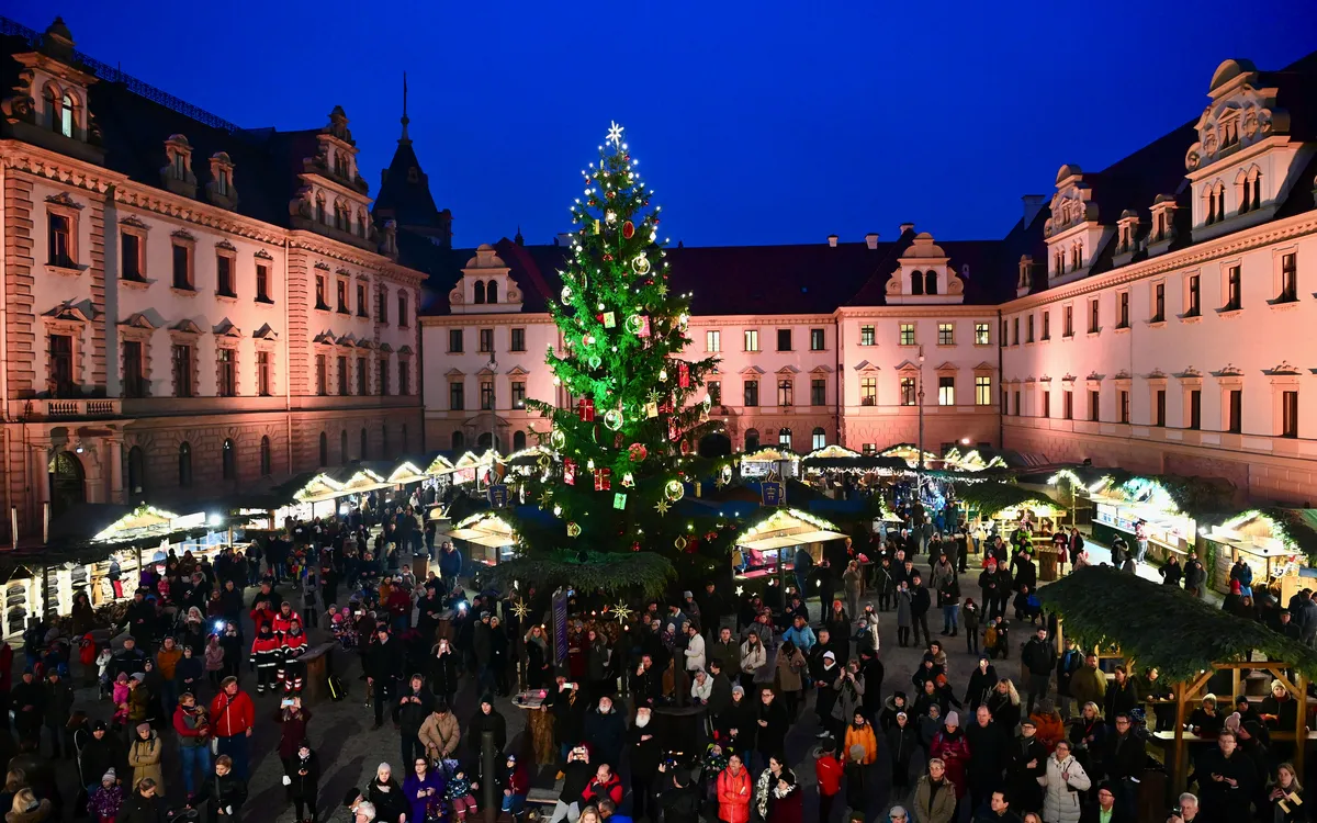 Weihnachtsmarkt am Abend mit großem Weihnachtsbaum und Menschenmengen in einem Innenhof