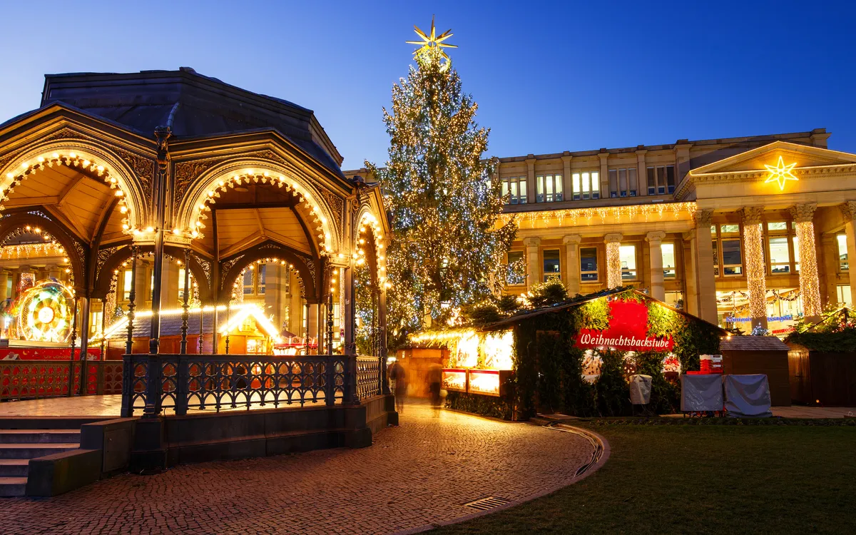 Weihnachtsmarkt mit Lichterdekoration und beleuchtetem Baum abends.