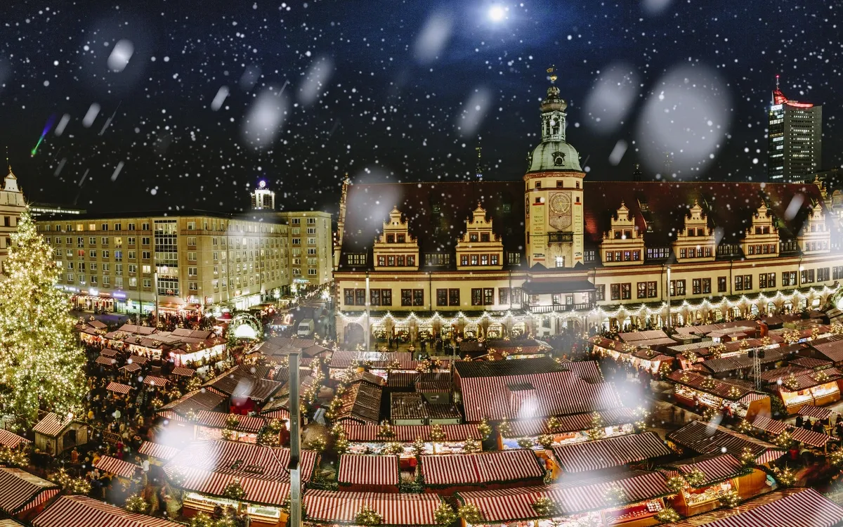 Weihnachtsmarkt bei Nacht mit Schnee und festlich beleuchteten Ständen in einer Stadt.